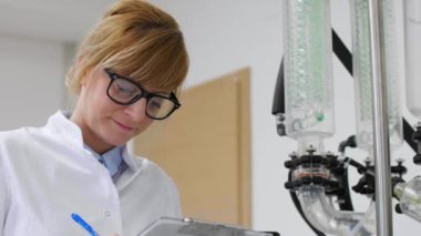 Bilim adamı CBD yağ çıkarma sırasında laboratuvarda rotovapor inceliyor. Lastik eldiven takıyor ve yeşil yoğunlaştırıcılı döner buharlaştırıcının yanında duruyor..