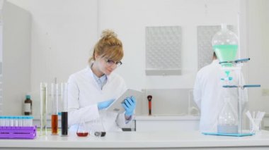 Laboratuvarda kenevir CBD, CBDA yağları ve tabletle çalışan iki bilim adamı. Lateks eldiven, cam tüpler ve erlenmeyer şişeleri kullanıyorlar. Esrar tohumlarından alınan sağlık hizmetleri eczanesi.