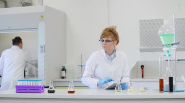 Laboratuvarda kenevir CBD, CBDA yağları ve tabletle çalışan iki bilim adamı. Lateks eldiven, cam tüpler ve erlenmeyer şişeleri kullanıyorlar. Esrar tohumlarından alınan sağlık hizmetleri eczanesi.