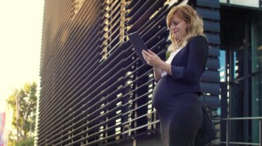 Tabletinde bir şeyler okurken modern bir binanın önünde duran gülümseyen bir iş kadını..