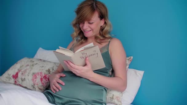 一个孕妇在床上半坐着 看书的时候她看起来很开心 她的一只手放在肚子上 — 图库视频影像