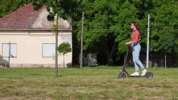 Mulher Bonita Jovem Monta Uma Scooter Elétrica Através Assentamento Urbano — Vídeo de Stock