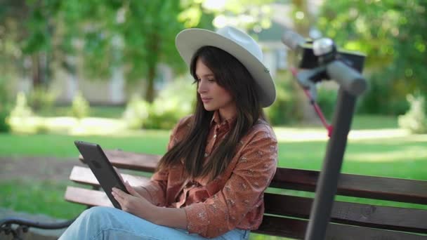 Una Joven Con Sombrero Sienta Banco Del Parque Desplaza Tableta — Vídeos de Stock