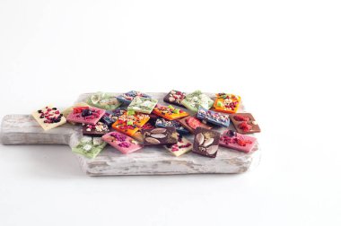 Farklı aromalı doğal Belçika çikolatası, kibrit çayı, yeşil, mavi, hindistan cevizi, üzerine meyve cipsi, fındık ve tohum serpiştirilmiş. Tahtada, beyaz arka planda. Boşluğu kopyala