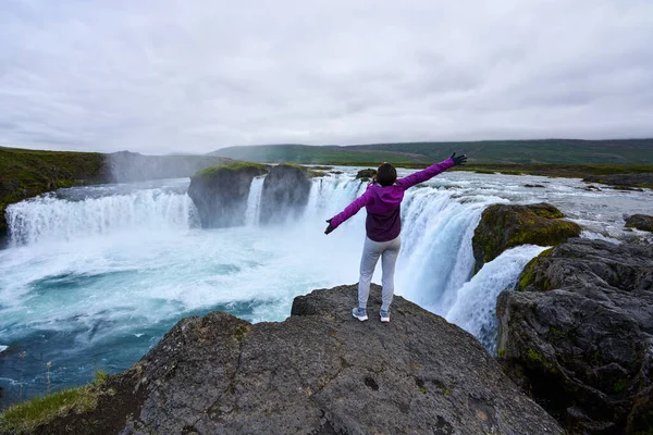 İzlanda 'da yeşillik ve güzel kayalarla Godafoss şelalesinin muhteşem manzarasına bakan bir kadın.