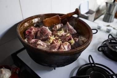 Kuzu etli antika güveç, sarımsak ve sobada pişirilirken ahşap havan.