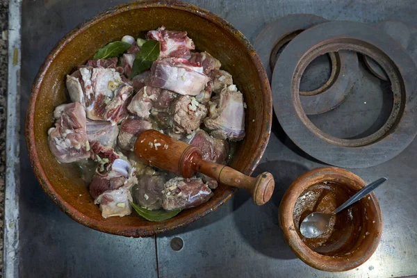 Eski bir güveçte, mutfakta pişirilen, ahşap bir havan topuyla sarımsak ve defne yaprağı ile tipik bir kuzu tarifi hazırlama manzarası.