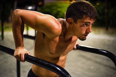 Gece antrenmanında üstsüz, kaslı genç adam eğitimi. Halka açık bir bar parkında. Daldırıyorum. Ön fotoğrafçılık.