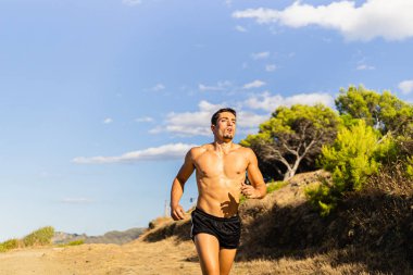 Genç sporcu bir patikada koşuyor. Fotoğraf, çok güneşli bir günde Akdeniz manzaralı cepheden çekildi. Gömleksiz model.