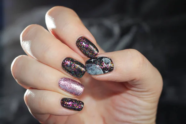 Black manicure with flames in the form of space, on the thumb there is a drawing of the planet Saturn and stars. Very effective design, background in tone to manicure - the Milky Way.