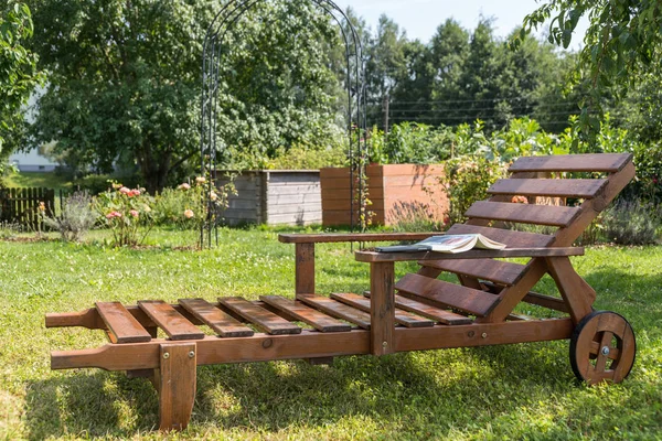 阳光躺椅用一本书在浪漫的花园里用木头做的 — 图库照片