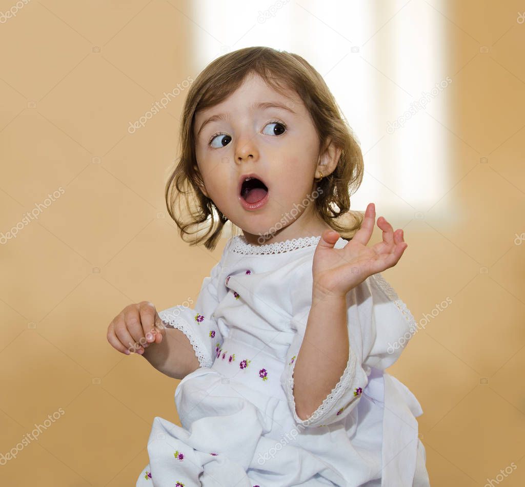 A little girl in a white dress looks surprised