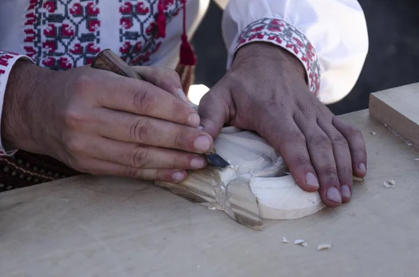 A man in a national shirt carves a wood ornament