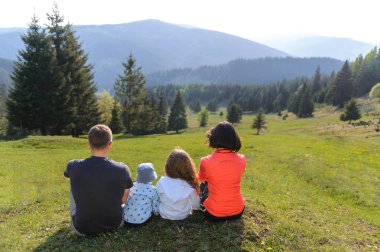Aile çimenlerin üzerinde oturan ve dağlar ve çam ormanı manzarayı