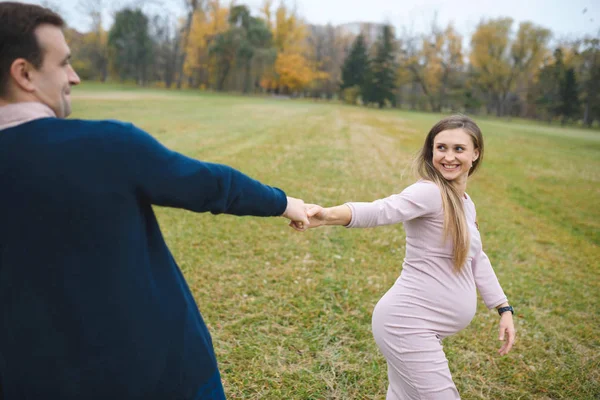 妊娠中の女性のドレスと屋外公園 カップルが手を繋いでいる笑顔で愛情のある夫 — ストック写真