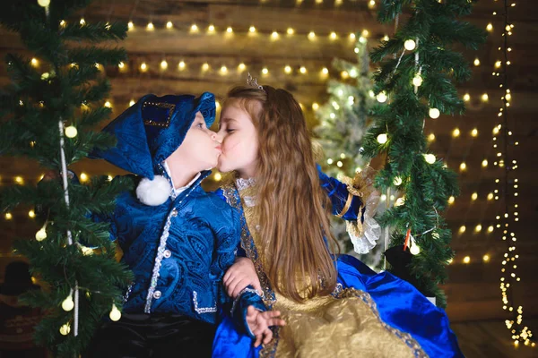 cute brother and sister in costumes kissing, little boy with girl sitting on swing in Christmas house