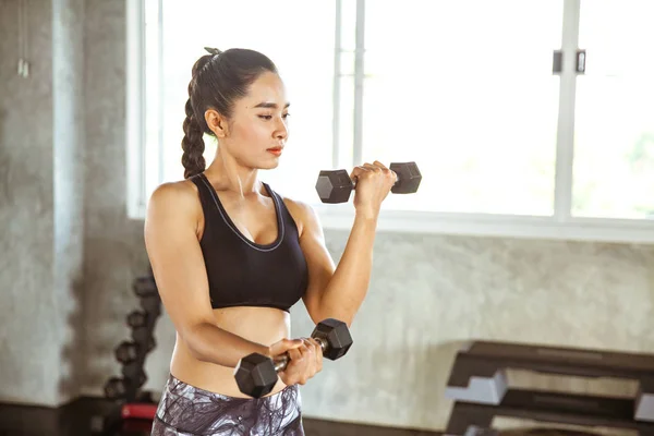 Young beautiful fitness woman holding dumbell in gym