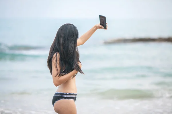 sexy bikini asian woman selfie with smart phone on tropical beac