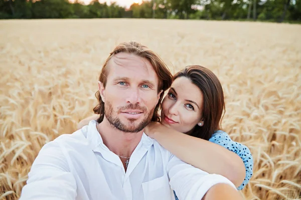 The beautiful couple embraces in the field of a rye and looks in a camera, the beautiful eyes, happy smiles, the long hair, an easy beard, wheat ears on background,  blue dress and white shirt