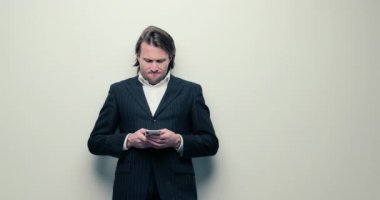 Siyah takım elbiseli yakışıklı adamlar cep telefonuna bakıyor. Uzun kıvırcık saçlı, beyaz gömlekli, iş adamı, tüccar, kazanan, çok şık, beyaz bir geçmişi var.