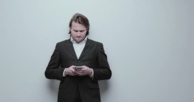 Siyah takım elbiseli yakışıklı adamlar cep telefonuna bakıyor. Uzun kıvırcık saçlı, beyaz gömlekli, iş adamı, tüccar, kazanan, çok şık, beyaz bir geçmişi var.