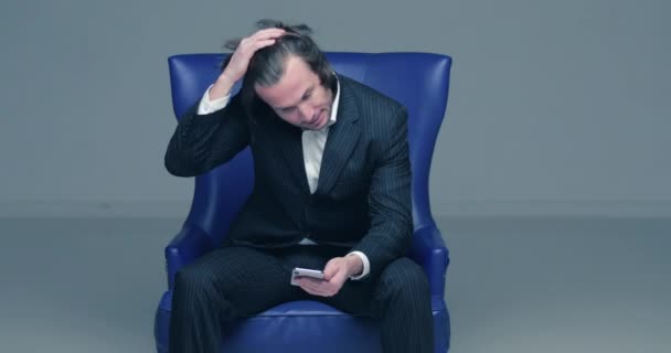 Przystojni Mężczyźni Czarnych Garniturach Siedzi Niebieskim Skórzanym Fotelu Patrzy Telefon — Wideo stockowe