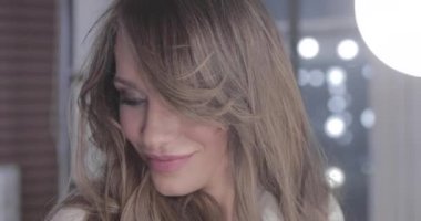 uzun kıvırcık saç flaunts ile güzel genç kız ve bir ayna önünde kapalı gösterir, flört, flört, gülümsüyor, boğucu bakmak, mutlu, kendini memnun, güzel makyaj, seksi dudaklar