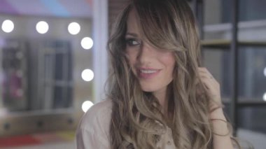 uzun kıvırcık saç flaunts ile güzel genç kız ve bir ayna önünde kapalı gösterir, flört, flört, gülümsüyor, boğucu bakmak, mutlu, kendini memnun, güzel makyaj, seksi dudaklar