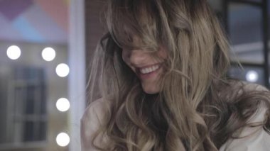 uzun kıvırcık saç flaunts ile güzel genç kız ve bir ayna önünde kapalı gösterir, flört, flört, gülümsüyor, boğucu bakmak, mutlu, kendini memnun, güzel makyaj, seksi dudaklar