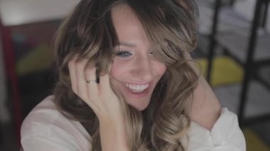 uzun kıvırcık saç flaunts ile güzel genç kız ve bir ayna önünde kapalı gösterir, flört, flört, gülümsüyor, boğucu bakmak, mutlu, kendini memnun, güzel makyaj, seksi dudaklar