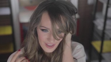 uzun kıvırcık saç flaunts ile güzel genç kız ve bir ayna önünde kapalı gösterir, flört, flört, gülümsüyor, boğucu bakmak, mutlu, kendini memnun, güzel makyaj, seksi dudaklar