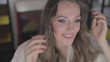 uzun kıvırcık saç flaunts ile güzel genç kız ve bir ayna önünde kapalı gösterir, flört, flört, gülümsüyor, boğucu bakmak, mutlu, kendini memnun, güzel makyaj, seksi dudaklar