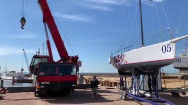 Rusya, St.Petersburg, 26 Mayıs 2020: Herkül Limanı, büyük endüstriyel vinç yelkenliyi kaldırır ve yüzdürür, yelkencilik mevsiminin başlangıcı, arka planda bir gökdelen, yelkenli yersizdir