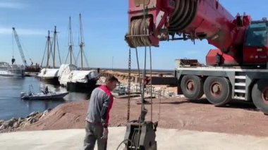 Rusya, St.Petersburg, 26 Mayıs 2020: Küçük yelkenli teknelerin kaldırılması ve suya inişleri için büyük bir endüstriyel vinç hazırlıyor, vinç yöneticisi vinci çalışmaya hazırlıyor