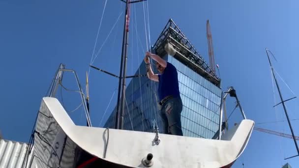 Россия, Санкт-Петербург, 26 мая 2020 года: Человек на яхтенной палубе готовит лодку для подъема парусника на большой промышленный кран — стоковое видео