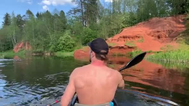 Russia, Gatchina, 29 maggio 2020: I giovani con un cappello galleggiano su un kayak sul fiume foresta, il bellissimo paesaggio, il fiume tranquillo, un tempo soleggiato, attivamente remate con un remo, bellissimo riflesso — Video Stock