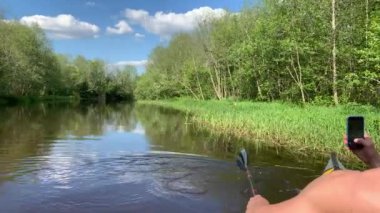 Rusya, Gatchina, 29 Mayıs 2020: Orman nehrinde bir kanoda yüzen iki genç adam, telefonla bir leyleğin videosunu çekiyor, güzel bir manzara, sakin bir nehir, güneşli bir hava.