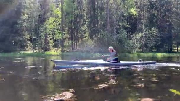 Rusland, Gatchina, 29 mei 2020: De jonge mannen met een kap drijven op een kajak op de bosrivier, het prachtige landschap, de rustige rivier, een zonnig weer, actief rijdend met een roeispaan, mooie reflectie — Stockvideo