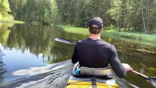 Ryssland, Gatchina, 29 maj 2020: De unga männen i mössa flyter på en kajak på skogsfloden, det vackra landskapet, den lugna floden, ett soligt väder, aktivt rader med en åra, vacker reflektion — Stockvideo