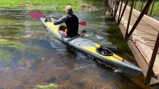 Russie, Gatchina, 29 mai 2020 : Les jeunes hommes en bonnet flottent sur un kayak sur la rivière de la forêt, le beau paysage, la rivière calme, un temps ensoleillé, se rangent activement avec une rame, beau reflet — Video