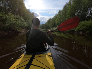 Şapkalı adamlar ormanın sakin nehrinde bir kanoda yüzerler, güzel bir manzara, değişken bir hava, kürek ve güzel bir yansımayla aktif olarak kürek çekerler.