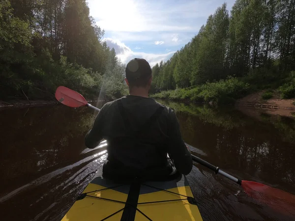 The men in a cap floats on a kayak on the forest quiet river, the beautiful landscape, a changeable weather, actively rows with an oar, beautiful reflection — Stock Photo, Image