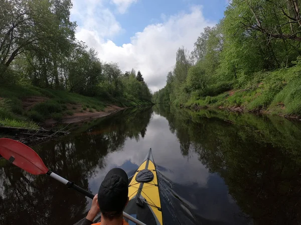 Die Männer mit der Mütze schwimmen auf einem Kajak auf dem ruhigen Fluss des Waldes, die schöne Landschaft, das wechselhafte Wetter, aktiv rudert mit einem Ruder, schönes Spiegelbild — Stockfoto