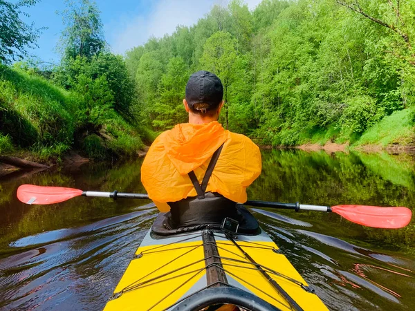 Los hombres en una gorra y impermeable de color naranja flota en un kayak en el río tranquilo bosque, el hermoso paisaje, un clima cambiante, filas activamente con un remo, hermoso reflejo —  Fotos de Stock