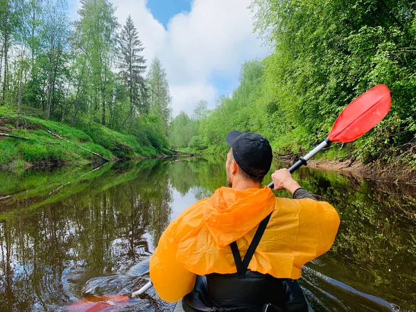 Los hombres en una gorra y impermeable de color naranja flota en un kayak en el río tranquilo bosque, el hermoso paisaje, un clima cambiante, filas activamente con un remo, hermoso reflejo —  Fotos de Stock