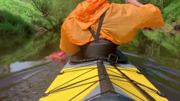 Rússia, Kirishi, 25 de maio de 2019: Os homens em uma tampa e capa de chuva de carros alegóricos de cor laranja em um caiaque no rio tranquilo floresta, a bela paisagem, um clima mutável, filas ativamente com um remo — Vídeo de Stock