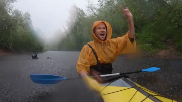 Ryssland, Kirishi, 25 maj 2019: Männen i en regnrock av orange färg flyter på en kajak på den lugna skogen floden, det vackra landskapet, ett regnigt väder, aktivt rader med en åra — Stockvideo