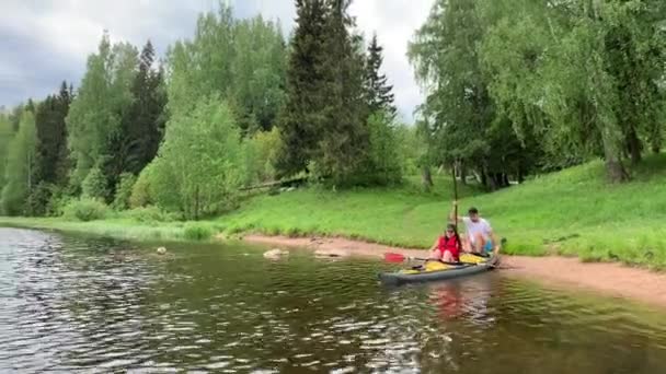 Oroszország, Gatchina, 2020. június 07.: Pár leereszti a kajakot a folyó vizén az erdőben, a gyönyörű tájat, a napos időjárást, aktívan evez egy evezővel, gyönyörű reflexióval, napsütéssel — Stock videók