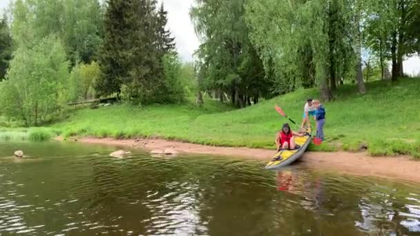 Oroszország, Gatchina, 2020. június 07.: Pár leereszti a kajakot a folyó vizén az erdőben, a gyönyörű tájat, a napos időjárást, aktívan evez egy evezővel, gyönyörű reflexióval, napsütéssel — Stock videók