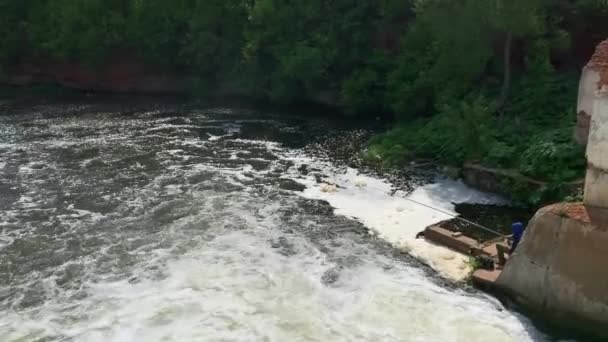 낚시꾼은 폭포에 앉아, 숲 속의 화창 한 날씨에 작은 댐 에 물이 빠른 속도로 흐르고 있다 — 비디오